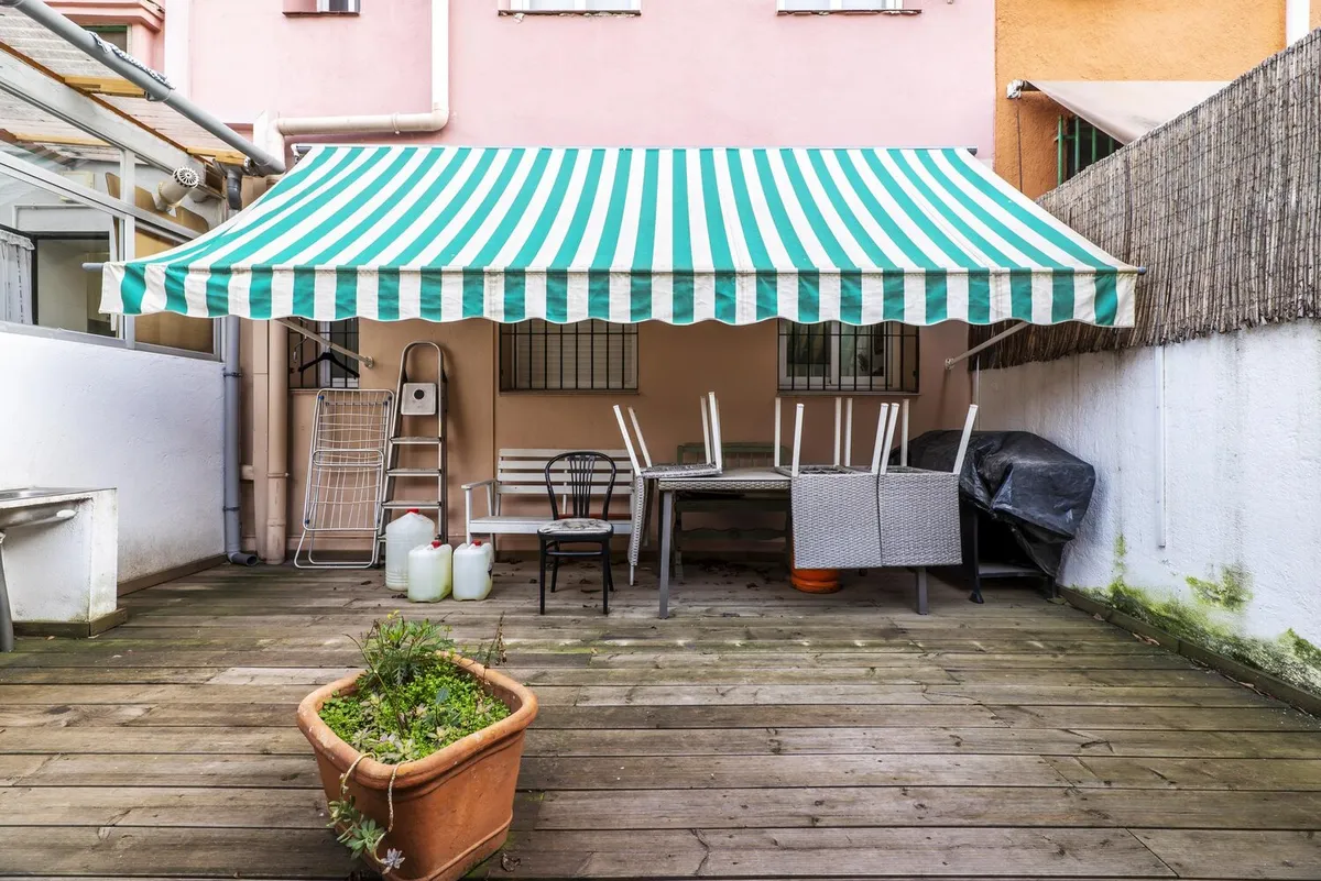 Store banne à rayures vertes et blanches déployé au-dessus de la terrasse en bois d'une maison de ville